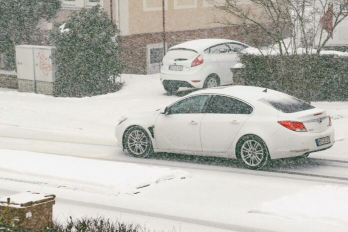 Two white cars driving on a snowy street.